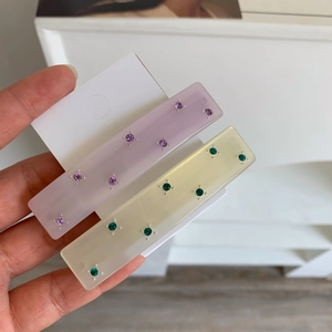 Close-up of rectangular acetate spring clips with colorful rhinestones in hand