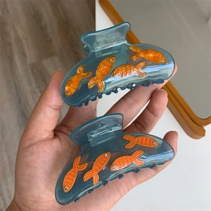 Détail de pinces à cheveux en acrylique bleu avec motifs de poissons orange et strass