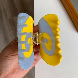 Detailed close-up of large blue and yellow swirl acetate hair claw clip with golden spring