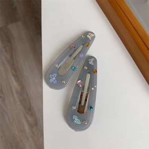 Detail view of two dark grey butterfly hair clips with colorful rhinestones on white background