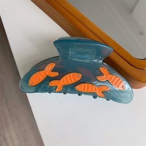 Détail d'une pince à cheveux en acrylique bleu avec poissons orange et strass étincelants