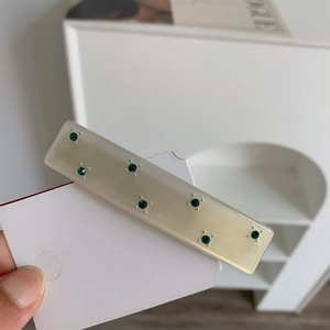 Detail of cream acetate hair clip with emerald green rhinestones in geometric pattern