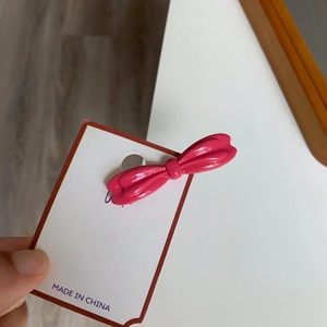 Détail d'une barrette à cheveux nœud en métal rose vif sur sa carte de présentation