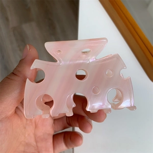 Détail de la pince à cheveux en résine rose marbrée avec design ajouré type fromage