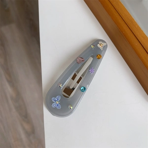 Macro detail of grey teardrop hair clip with colorful rhinestones and butterfly patterns