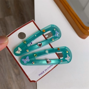 Detail showing two butterfly hair clips in teal resin with colorful rhinestones