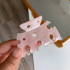 Détail du clip à cheveux en acétate rose avec motif ajouré circulaire et reflets de perle