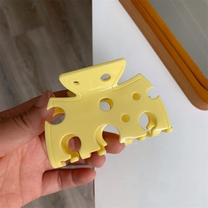 Vue détaillée d'une pince à cheveux créative en forme de fromage jaune tenue à la main