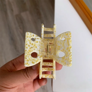Détail de la pince à cheveux papillon avec texture marbrée jaune et ressort doré