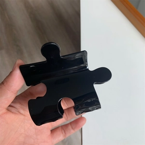 Detailed view of creative puzzle-shaped black hair claw clip with a glossy finish