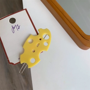 Détail d'une pince à cheveux en résine jaune forme fromage avec trous sur carte support