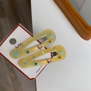 Detail of two yellow resin butterfly hair clips with colorful rhinestones on card