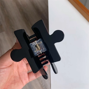 Detail view of creative black jigsaw puzzle hair claw clip held by hand for hairstyle