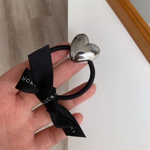 Close-up of black elastic hair tie with silver heart metal and Lucky printed bow