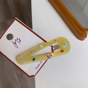 Detailed macro of a yellow resin hair clip with rhinestones and blue butterfly on a card