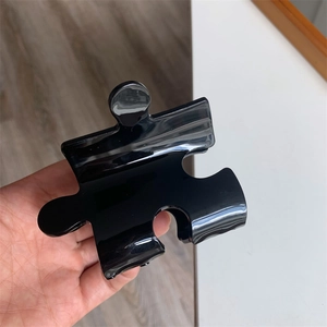 Detail view of a black puzzle-shaped hair claw clip with a glossy finish and creative design
