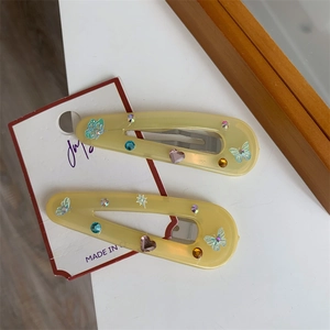 Close-up of yellow resin hair clips with butterfly prints and colorful rhinestones on card
