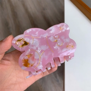 Detail of hand-held pink acetate hair claw clip with marbled texture and gold accents
