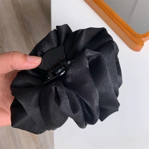 Détail de la texture en satin noir et des grands plis sur cette pince à cheveux fleur
