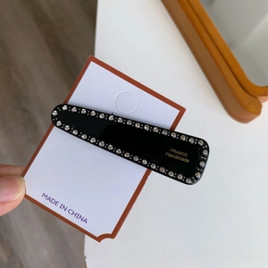 Barrette noire minimaliste avec cristaux et lettrage doré sur carte de présentation
