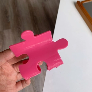 Close-up of bright pink puzzle-shaped acetate hair claw clip with a glossy finish