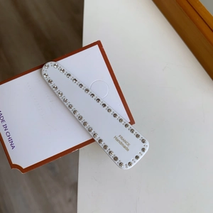 Détail de la pince à cheveux rectangulaire blanche avec bordure en cristal et texte doré