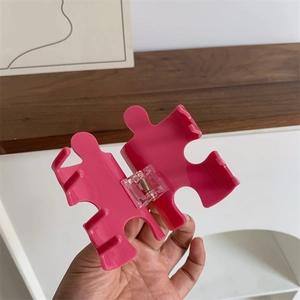 Detail view of a pink puzzle-shaped acetate hair claw clip with a strong metal spring