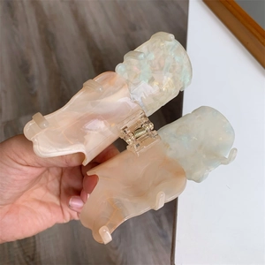 Detail view of large acetate hair claw with two-tone marble texture and golden spring