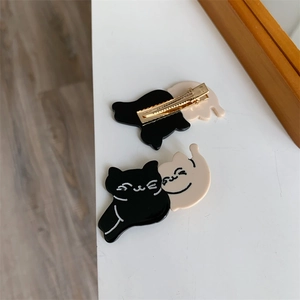 Close-up of cat-shaped hair clips in black and beige with metallic duckbill clamps