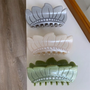 Three pearl-studded acetate hair claws in grey, beige, and green shown from a top view