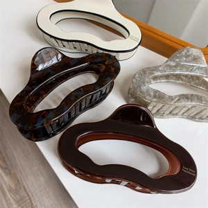 Detail showing four assorted acetate hair claws with wavy edges and brand printing