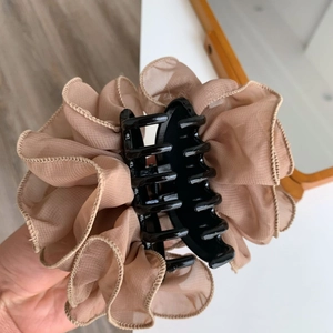Close-up of elegant beige ruffle mesh fabric detail on a black plastic hair claw clip