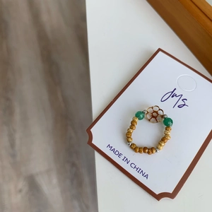 Détail d'une bague en perles avec breloque fleur dorée et perles en bois naturel
