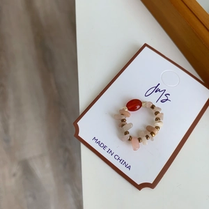 Détail d'une bague en perles d'agate rouge et de quartz rose sur son support de vente