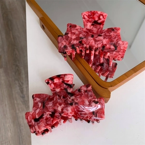 Détail d'une pince à cheveux en acétate marbré rouge reflétée dans un miroir chic