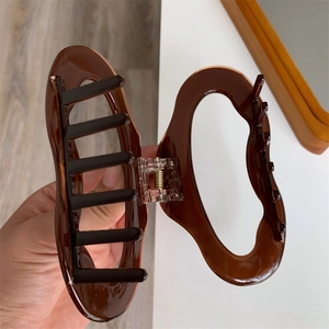 Macro detail of dark brown wave cellulose acetate hair claw clip with strong metal spring