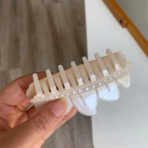Detail of cream acetate hair claw with row of pearls held by hand for scale