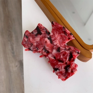 Détail d'une pince à cheveux en acétate marbré rouge avec grand nœud et prise sécurisée