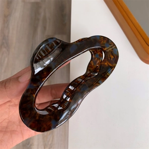 Detail showing high-gloss acetate hair claw clip with tortoise pattern and handmade logo
