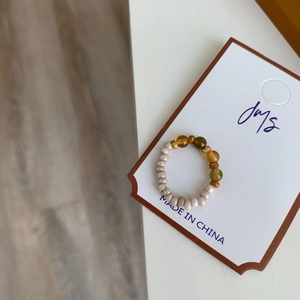 Gros plan d'une bague élastique perlée avec des perles blanc nacré, ambre et vert olive