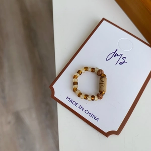 Bague perlée faite main avec pierres ambrées et perle en bois sculptée sur surface blanche