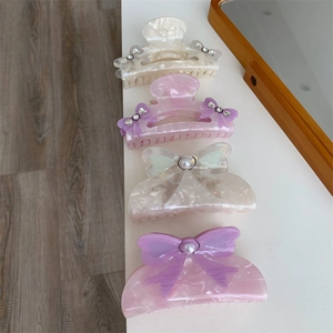 Detail of four elegant acetate bow hair claws with pearls and rhinestones in soft colors