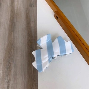 Gros plan d'une pince à cheveux en acétate à rayures bleues et blanches sur table
