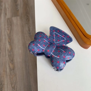 Détail de la pince à cheveux noeud en denim bleu avec des pois rouges sur blanc