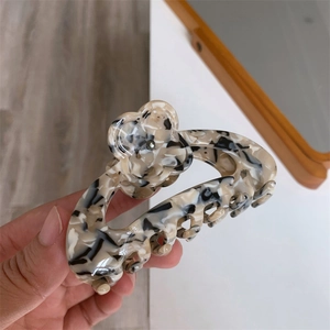 Detail shot of marble-patterned hair claw clip with floral decoration in woman's hand