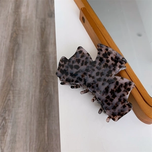 Gros plan d'une pince à cheveux en acétate motif écaille sur un bureau blanc