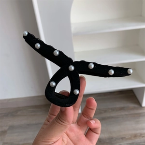 Detail of elegant black velvet hair claw clip with cross-twist design and white pearls