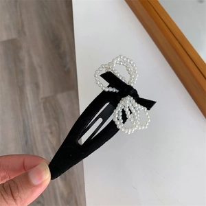 Detail of a black flocked hair clip featuring a white faux pearl bow on a metal base