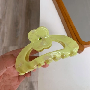 Close-up of a floral acetate hair claw clip with green rhinestone center and marble texture