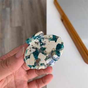 Détail de la pince à cheveux en acétate en forme de coquillage avec motifs bleus et strass